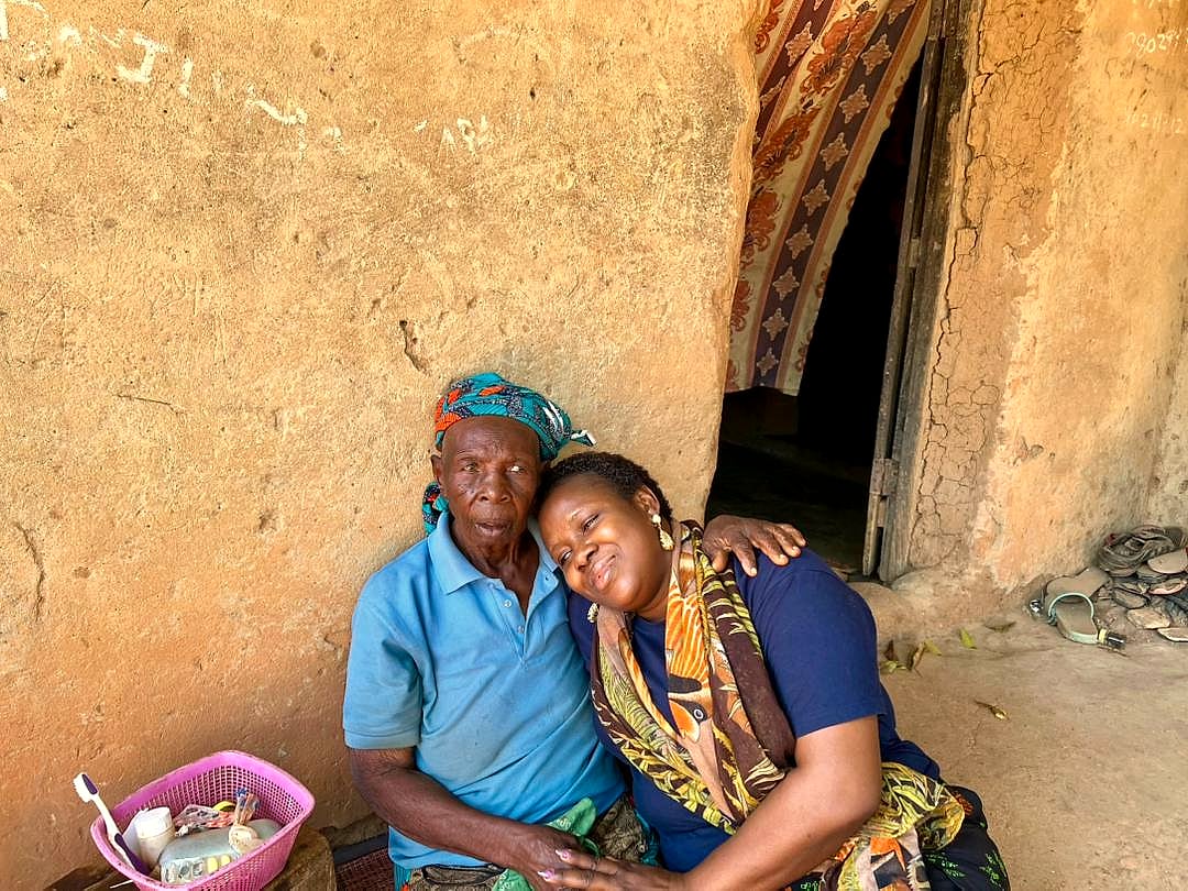 A volunteer resting her head on an elderly woman's shoulder