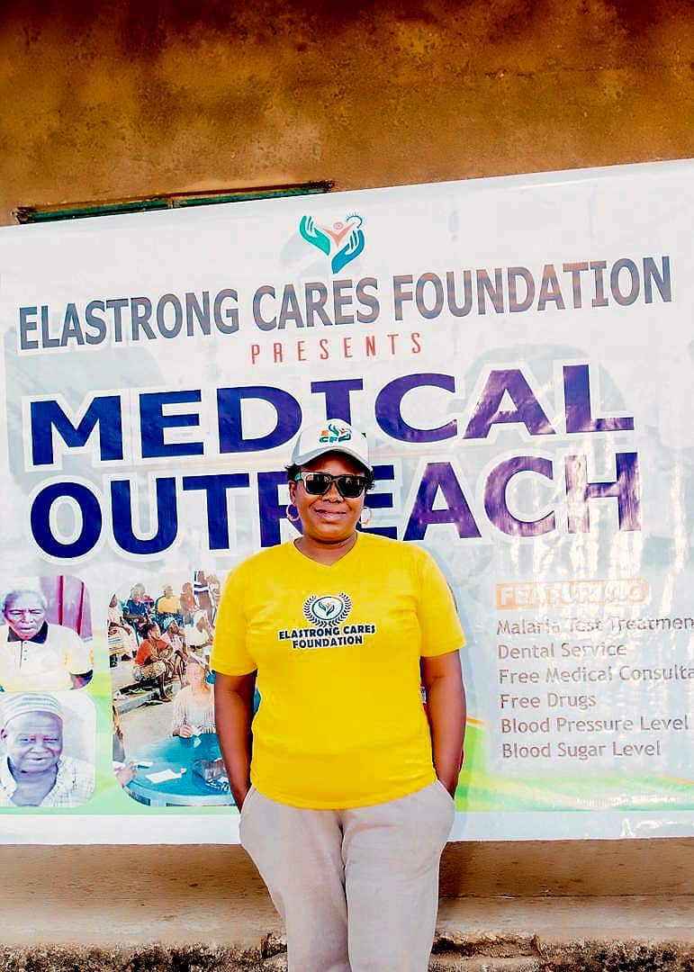 A volunteer in front of the Elastrong Cares Foundation Medical Outreach banner